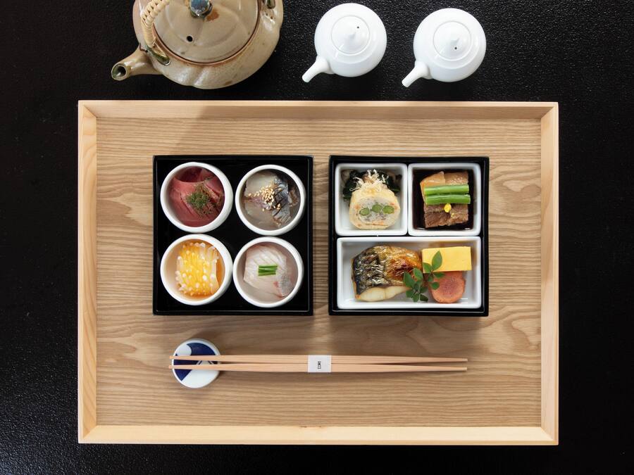 A wooden tray with various Japanese dishes, chopsticks, and two teapots.