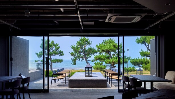 A modern interior with a view of the sea, featuring a seating area with tables and chairs, a central lantern, and a stone floor. - ONCRI-KARATSU (Karatsu)