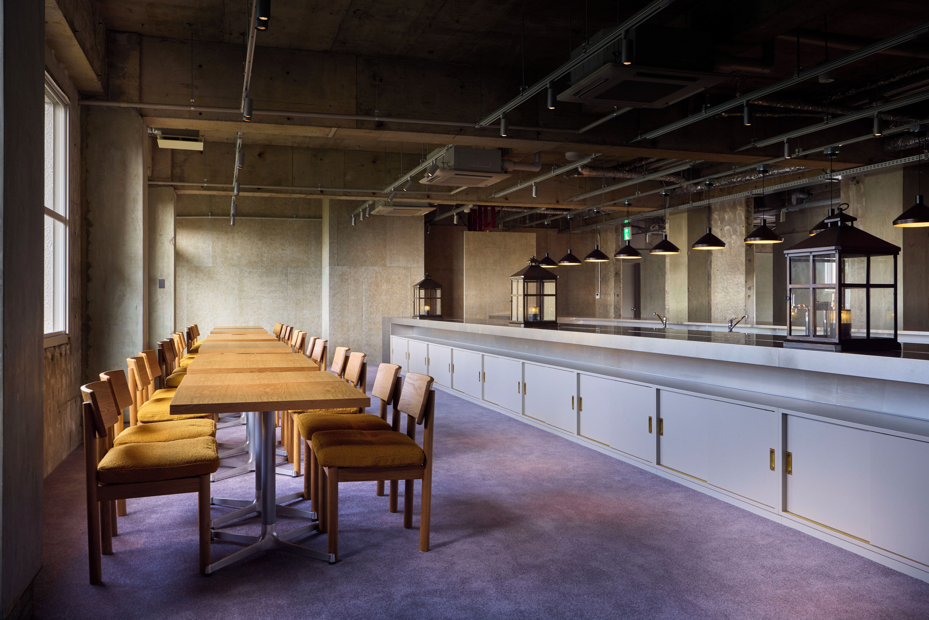 A conference room with a long table and chairs, white cabinets, and pendant lighting.