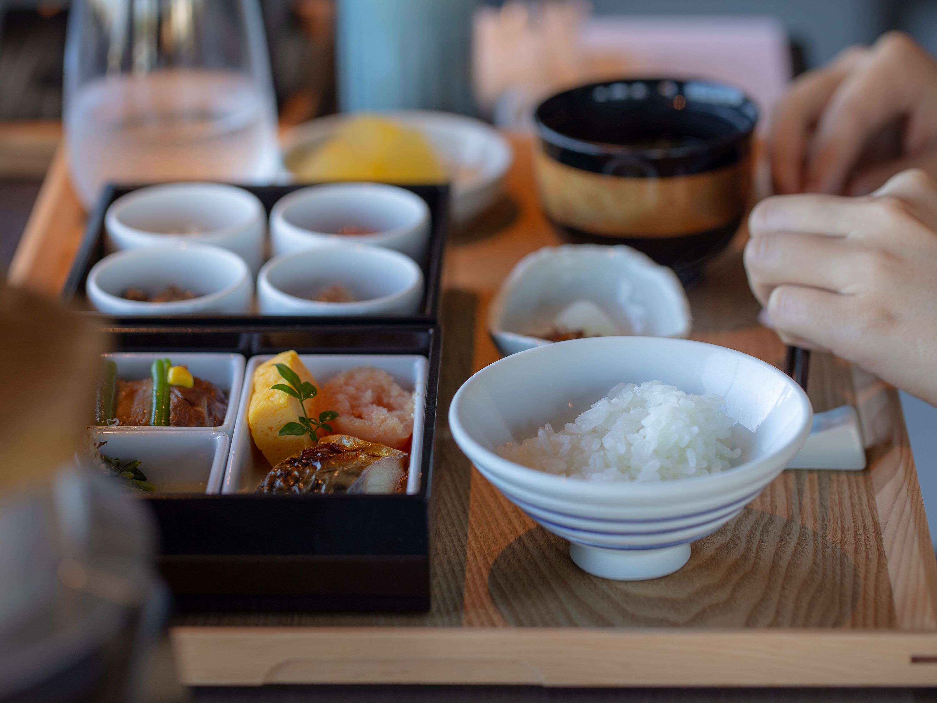 A traditional Japanese meal with various dishes including rice, fish, and vegetables, served on a wooden tray.