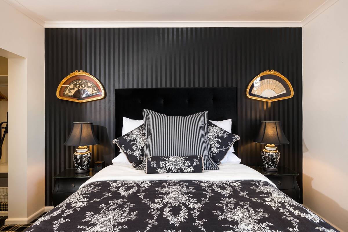 Une chambre à coucher bien rangée, avec une couvre-lit à motifs noir et blanc, un coussin rayé et deux tables de chevet dotées de lampes.