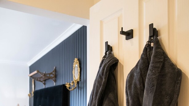 Un dormitorio con una cama, una mesita de noche, una lámpara y dos batas colgadas en una puerta.