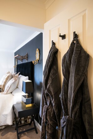 Un dormitorio con una cama, una mesita de noche, una lámpara y dos batas colgadas en una puerta.