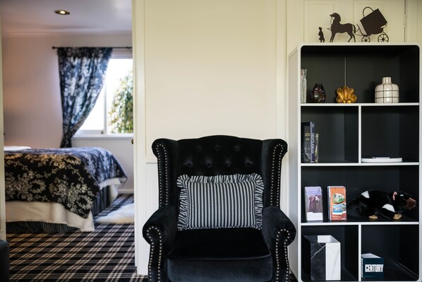 Una habitación con un sillón negro, una estantería, una cama con edredón floral y una ventana con cortinas.