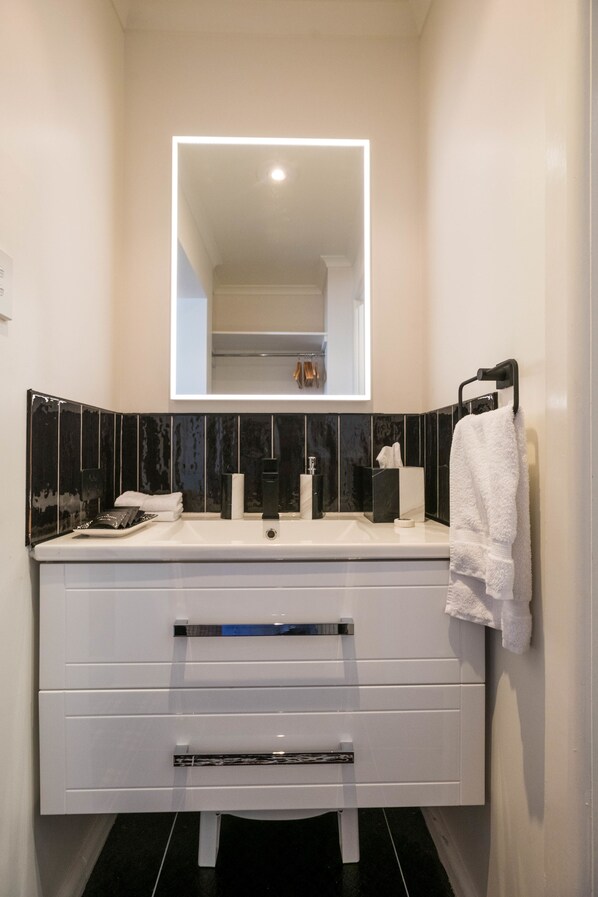 A modern bathroom with a white vanity, black and white tiles, a mirror, and a towel rack. - Battery Point Boutique Accommodation (Battery Point)