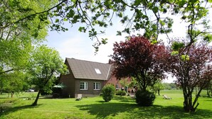 A house with a sloped roof, surrounded by a well-maintained lawn and a small pond. - Spacious vacation residence for 6 pers. with pool and garden. Sauna - shared use (Stadland-Reitland)