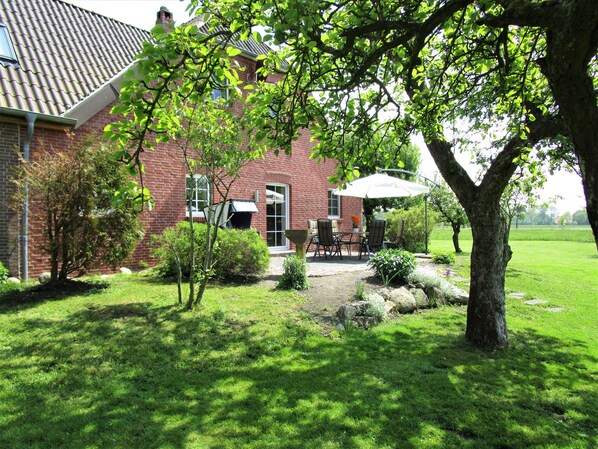 Une maison en briques avec un patio, un arbre et une pelouse.