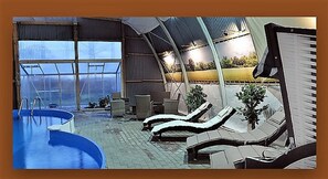 Un espace piscine doté de chaises longues et d’une partie fermée par des parois vitrées.