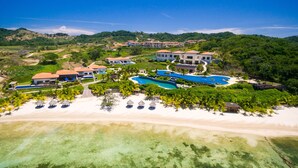 A resort with multiple swimming pools, beachfront villas, and a sandy beach.