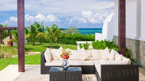 A covered outdoor seating area with a view of the ocean, a white sofa, and a table with a vase of flowers.