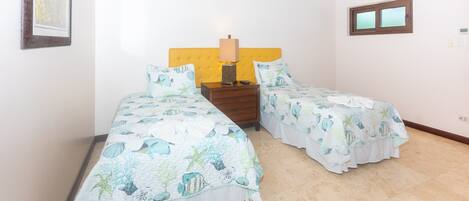 A bedroom with two beds, a nightstand, a lamp, and a window.