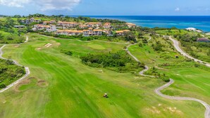 An aerial view of a golf course with multiple houses and a clear view of the ocean.