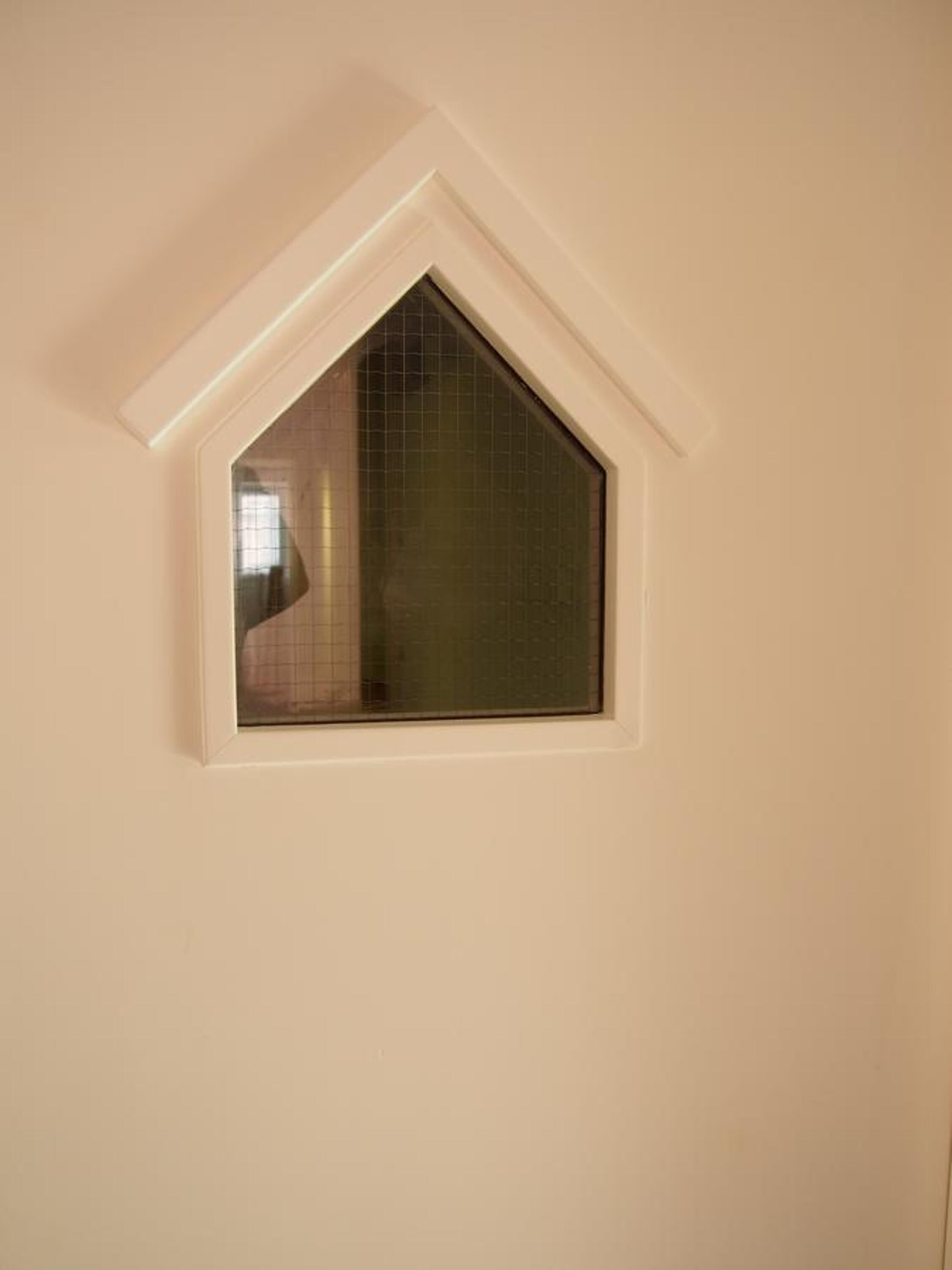 A small dormer window with a triangular design, set in a plain wall.