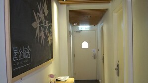 A hotel reception area with a wooden reception desk, a blackboard with text, and a hallway leading to an exit. - Ukkei Inn (Kowloon)