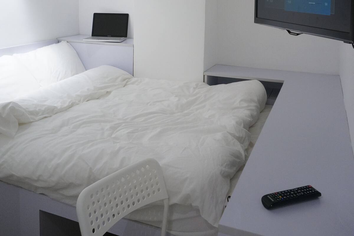 A modern bedroom with a bed, a desk, a chair, a TV, and a laptop.