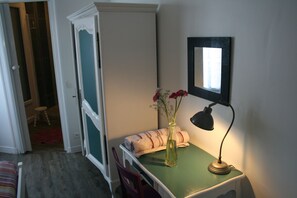 A room with a green table, a lamp, a mirror, and a vase with flowers.