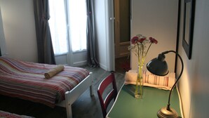 Una habitación con cama, una silla, un escritorio, una lámpara y un jarrón con flores.
