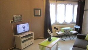 Una sala de estar con televisor, una mesita con un jarrón de flores, un sofá y una ventana con cortinas.