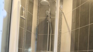 Una ducha con puerta de cristal, paredes azulejadas y un taburete blanco.