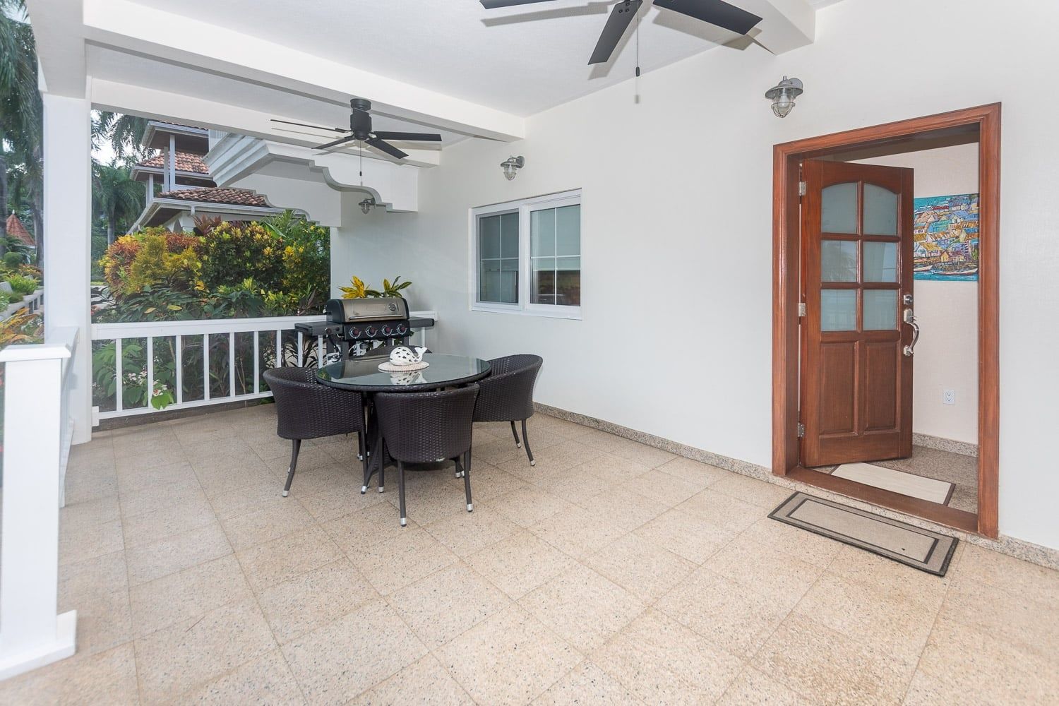 An outdoor patio with a round table and chairs, a grill, and a ceiling fan.