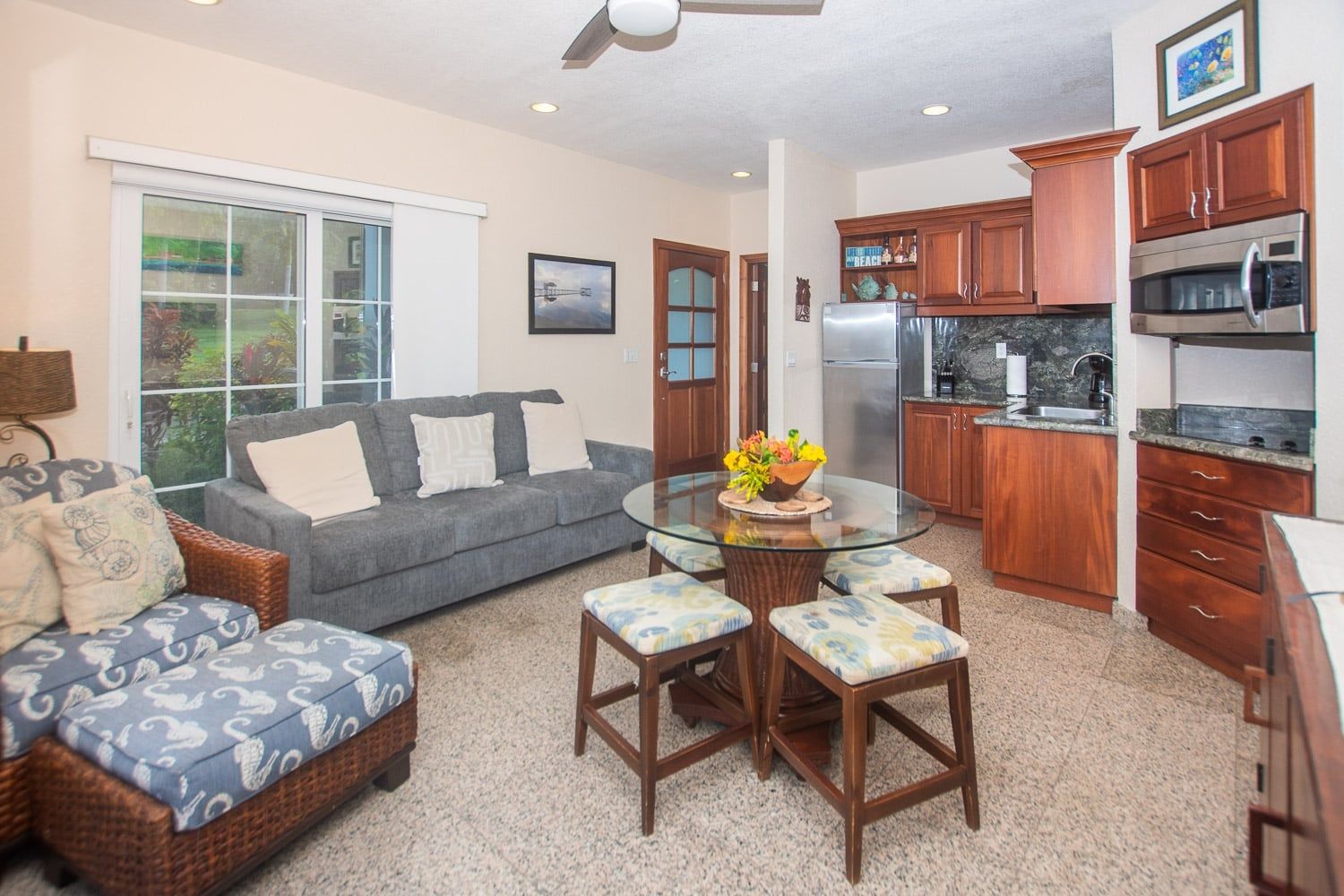 A compact living space with a sofa, a dining table with chairs, a kitchen area with wooden cabinets and appliances, and a large window.