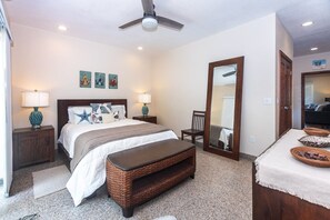 A hotel room with a bed, bedside tables, a mirror, a bench, and a ceiling fan. - Lawson Rock - Angelfish 100 (Roatan)