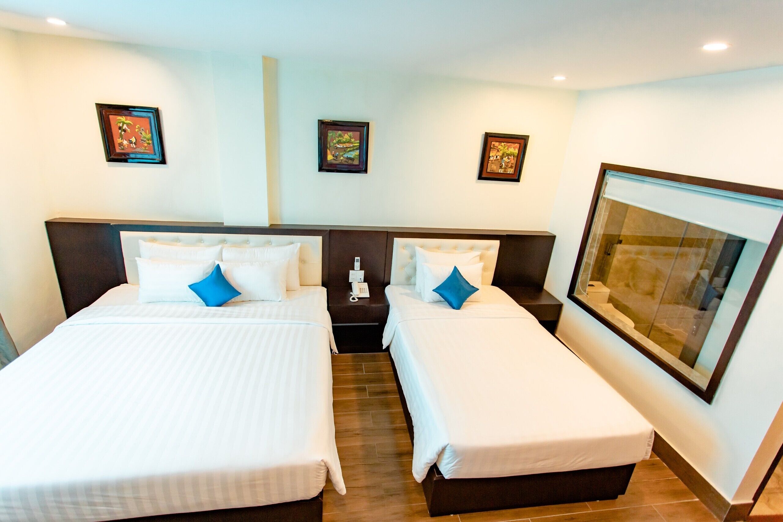 Habitación de hotel con dos camas, una mesita de noche con teléfono y cuadros enmarcados en la pared.