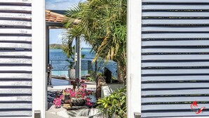 A view through a wooden door into a balcony with a pool, surrounded by potted plants and flowers. - Charming waterfront villa, labeled "4 * tourism furnished" (Le robert)