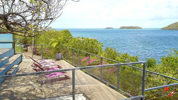 A deck with wooden flooring and metal railings overlooking a body of water with islands in the distance.