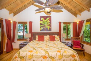 A bedroom with a bed, a chair, a ceiling fan, and windows with curtains. - Casa de Admirada (Roatan)