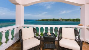 A balcony with two wicker chairs and a small table, overlooking a turquoise sea and a distant island. - Coral Vista #3 (Roatan)