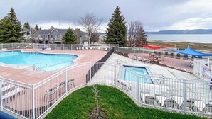 A pool area with a fenced deck, lounge chairs, and a view of a lake and mountains. - Inn Building Condo#113 - Ground Level, Pool Side (Garden City)