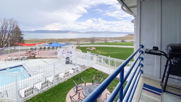 A balcony with a pool, outdoor seating, and a view of a park and mountains. - Inn Building Condo #203- Remolded with Lake View! (Garden City)
