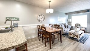 A modern kitchen with a granite countertop and wooden chairs, a dining table, and a clock on the wall. - Inn Building Condo #203- Remolded with Lake View! (Garden City)