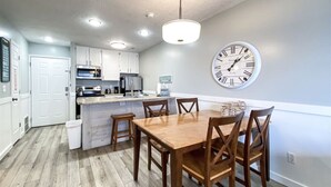 A modern kitchen with white cabinets, a central island, and a dining area with a wooden table and chairs. - Inn Building Condo #203- Remolded with Lake View! (Garden City)