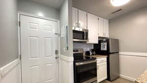 A compact kitchen with white cabinetry, a stainless steel refrigerator, a microwave, an oven, and a dishwasher. - Inn Building Condo #203- Remolded with Lake View! (Garden City)