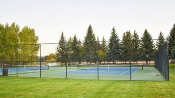 Cancha de tenis exterior con red, rodeada por una cerca y árboles.