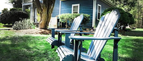 Deux fauteuils Adirondack dans un jardin, avec une maison bleue en arrière-plan.