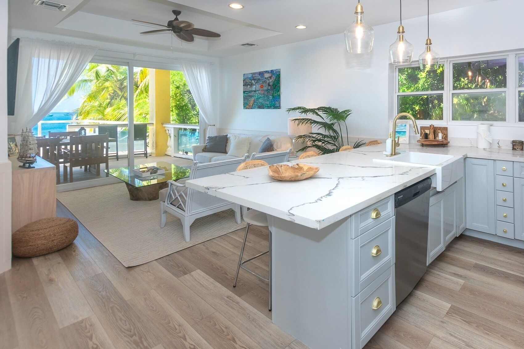 A modern kitchen with a large island, a dining area with a view, and a ceiling fan.