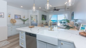 A modern kitchen with a large island, pendant lighting, and a view of the ocean. - Villa Del Playa #2 (Roatan)