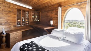 Un dormitori de cabanes de fusta amb un llit, un escriptori i una finestra gran que ofereix vistes del paisatge.