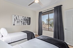 A bedroom with two beds, a ceiling fan, a window with curtains, and a door.