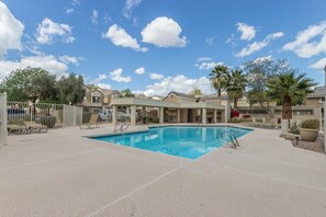 A pool area with lounge chairs and a covered seating area, surrounded by buildings and trees.