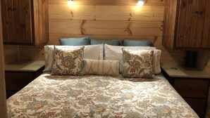 A bedroom with a wooden headboard, a floral-patterned bedspread, and multiple pillows.