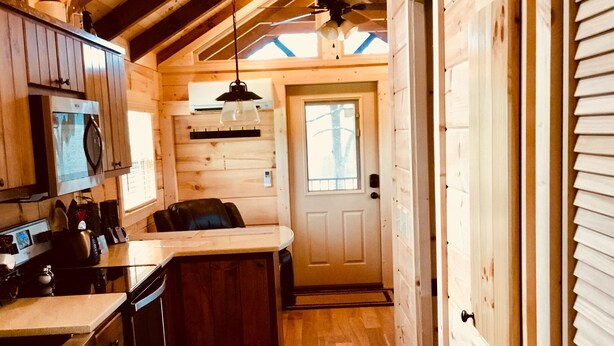 A wooden cabin interior with a kitchen, dining area, and a door leading to another room.