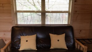 A wooden-framed black leather sofa with two beige cushions, positioned in front of a window with a view of trees.