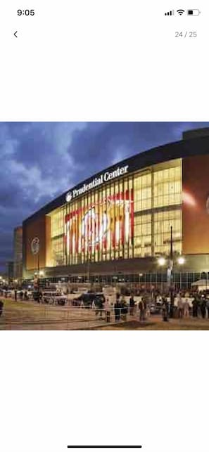 The exterior of the Prudential Center with a large illuminated sign, a spacious plaza, and a modern architectural design.