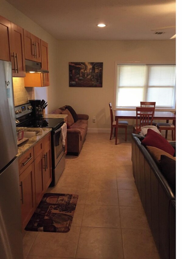 A compact kitchen with wooden cabinets, a refrigerator, stove, and a dining area with a table and chairs.