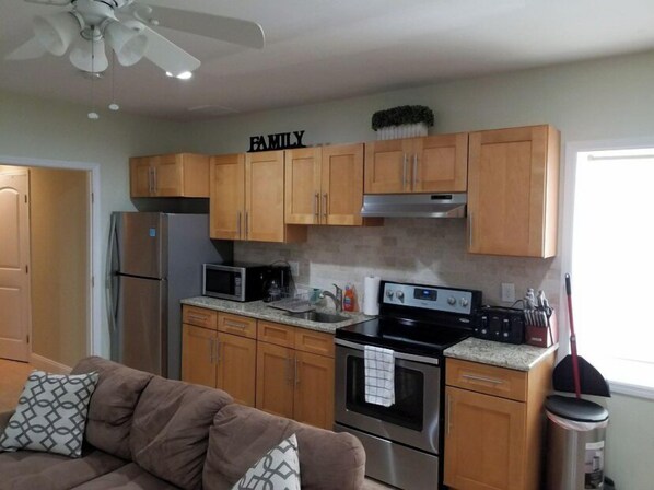 Cocina con armarios de madera, microondas, estufa y ventilador de techo.
