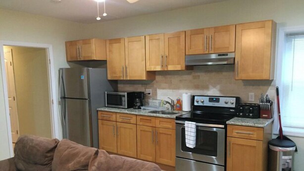 A compact kitchen with wooden cabinets, a stainless steel refrigerator, a microwave, an oven, and a sink. - 1 BR located 5 minutes away from St Joseph & Hackensack Hospital. 15 min to NYC  (Paterson)